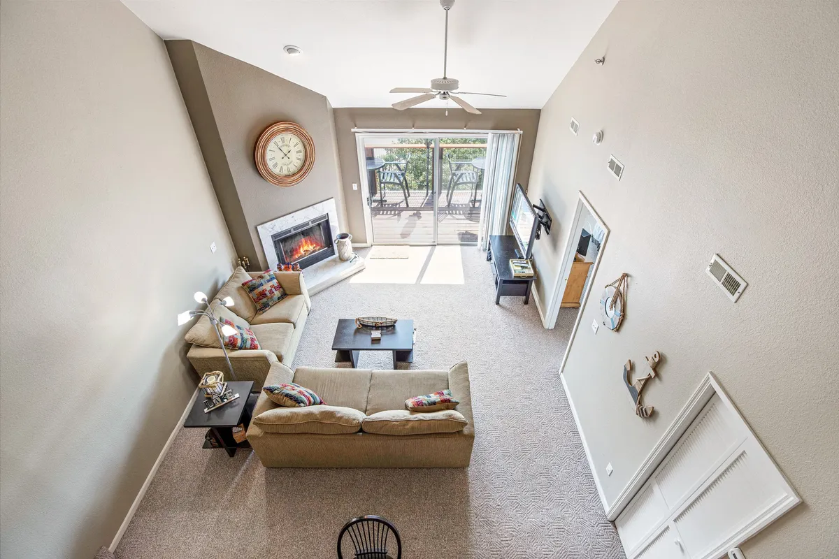 A welcoming living area featuring a plush sofa, a cozy fireplace, a large coffee table, and expansive windows looking out to the deck. The room is bathed in natural light, with a seamless transition to the outdoor space through glass doors, creating an inviting atmosphere for relaxation, socializing, and enjoying the lake views.