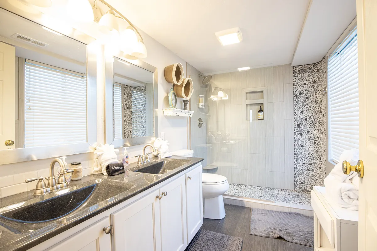 A modern, elegant ensuite bathroom featuring a double sink vanity, walk-in shower, and sophisticated decorative wall accents. The space appears clean, inviting, and designed for both relaxation and practicality.