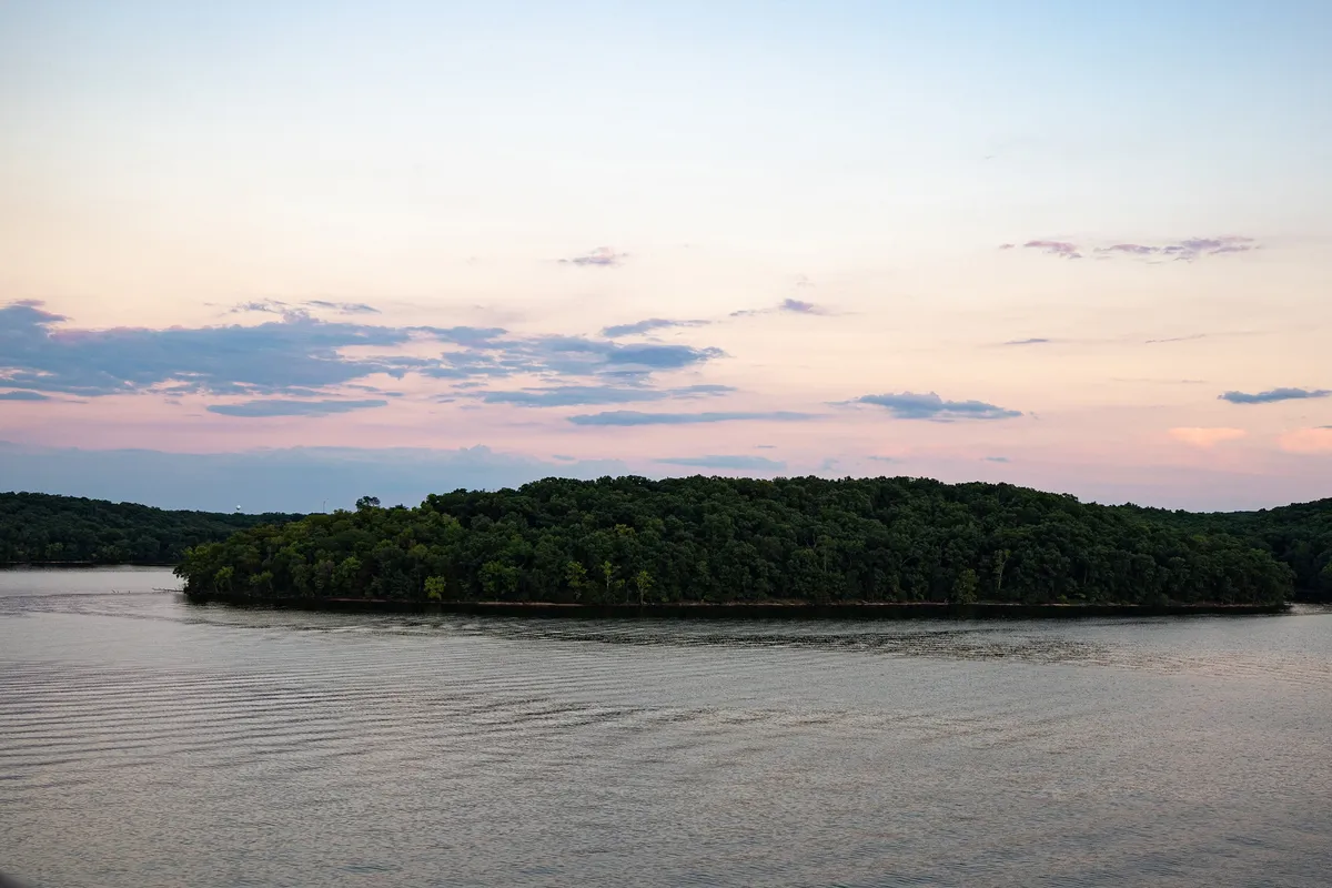 A tranquil lake view featuring a small island, glassy water, and expansive sky. The setting sun casts warm hues, making it perfect for boating, fishing, or simply relaxing and enjoying nature’s beauty throughout the year.
