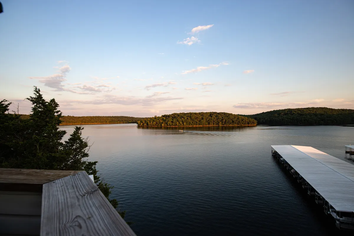 A tranquil view of calm lake water with a distant island and a wooden pier extending from the shore. The scene suggests activities like boating and fishing, and the peaceful setting is ideal for lakeside picnics or meals.