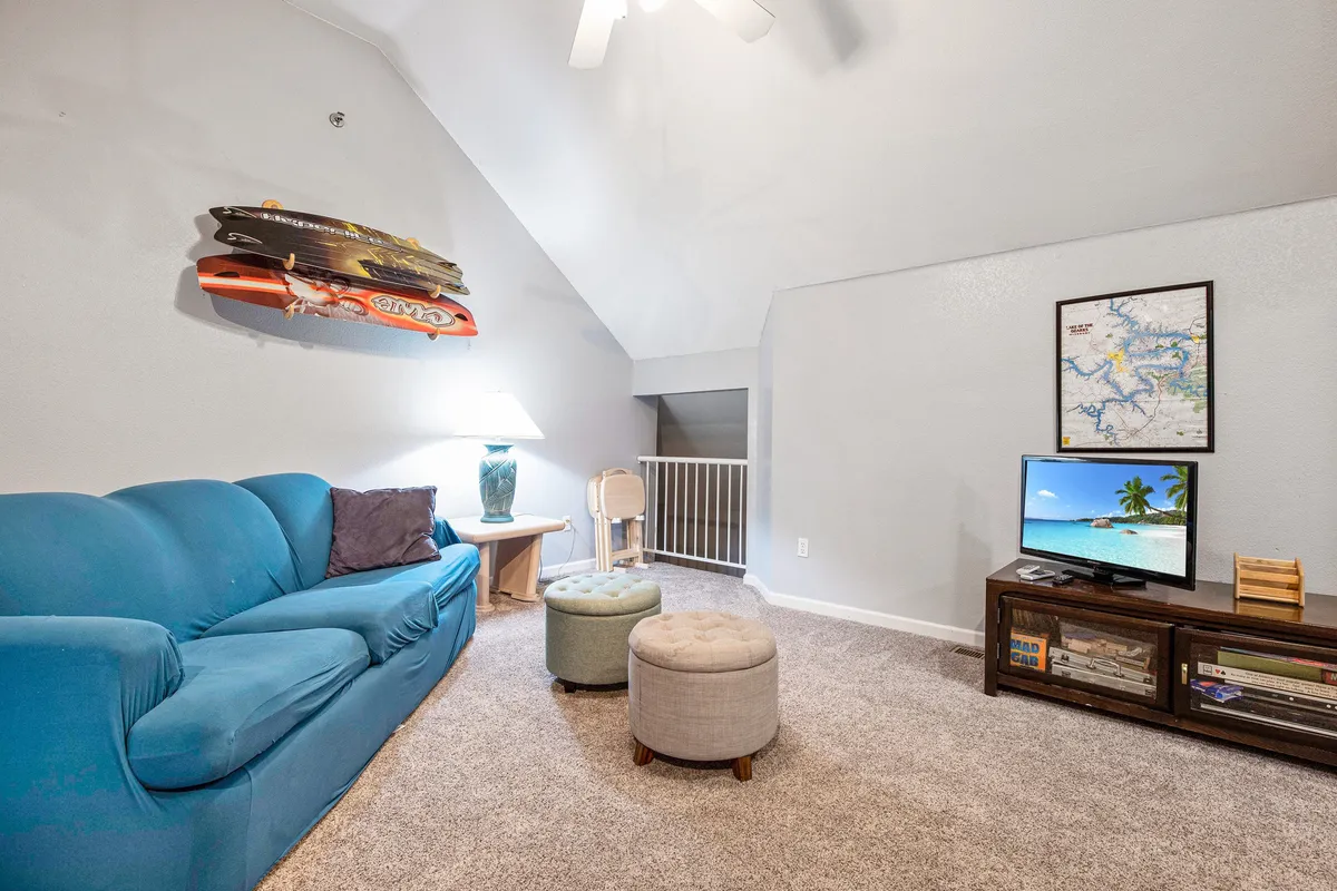 An inviting family room with a blue couch, wall-mounted surfboard, television, and decorative lamp. The room is casual and lively, perfect for both kids and adults to enjoy video games, TV, or creative downtime. The decor adds a playful touch, enhancing the youthful vibe.