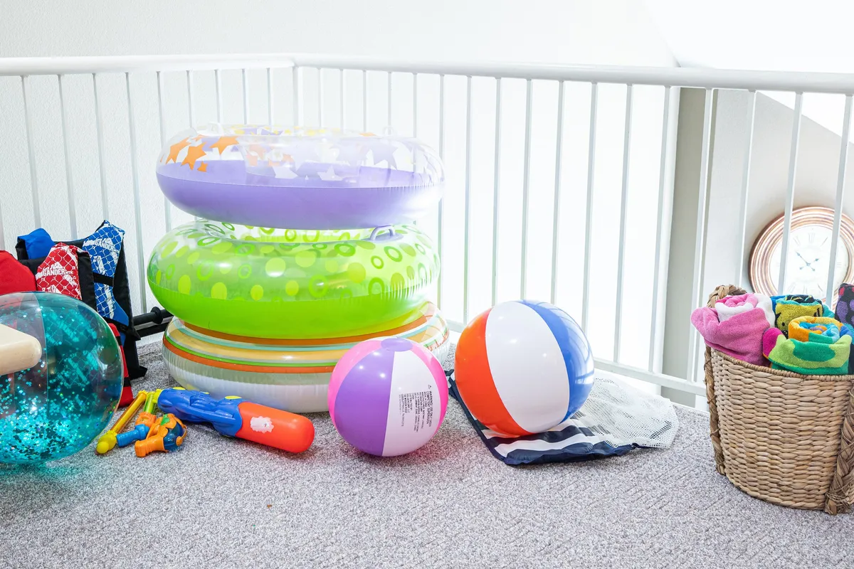 Inside, colorful inflatable rings, beach balls, and a basket of pool towels are arranged, ready for guests. The vibrant items evoke a sense of playful energy and thoughtful preparation for pool use.