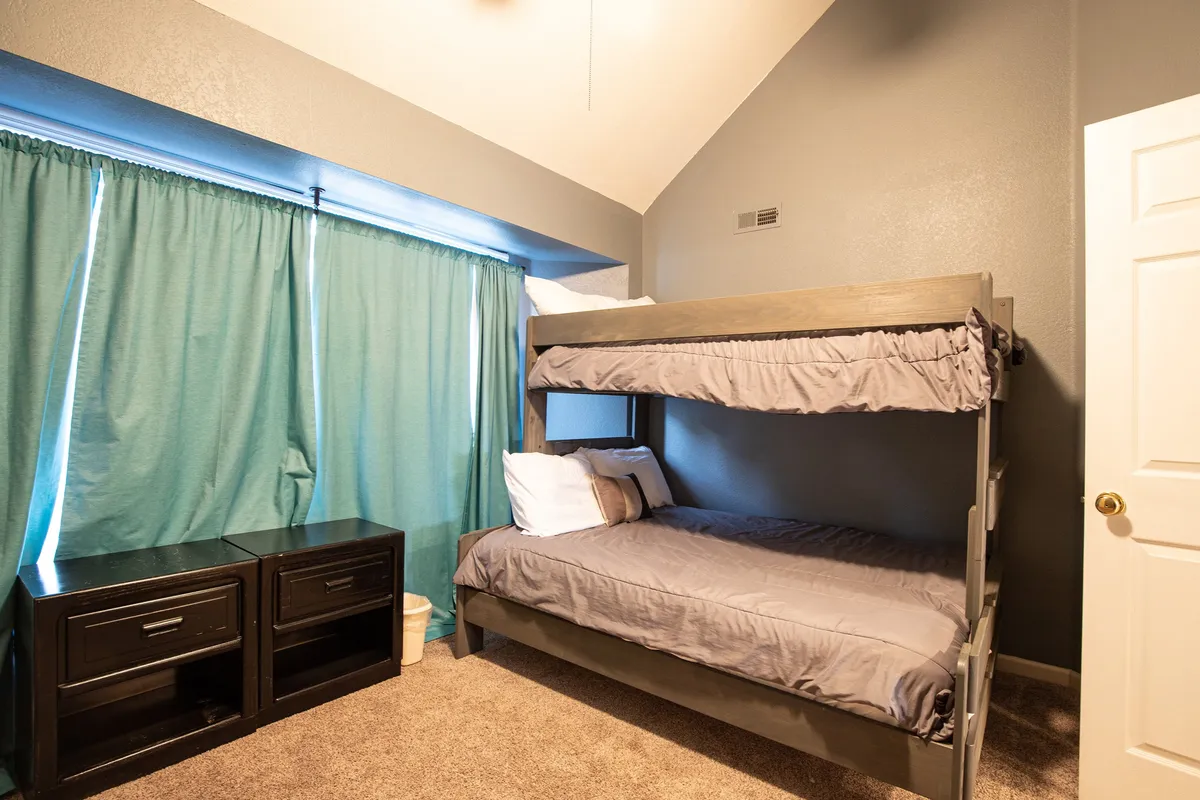 A kid-centric interior scene featuring a bunk bed, curtains, and a nightstand. The arrangement offers a cozy nook for children to play games, read, or relax after an active day. The space hints at comfort and togetherness, ideal for sleepovers or quiet afternoons.