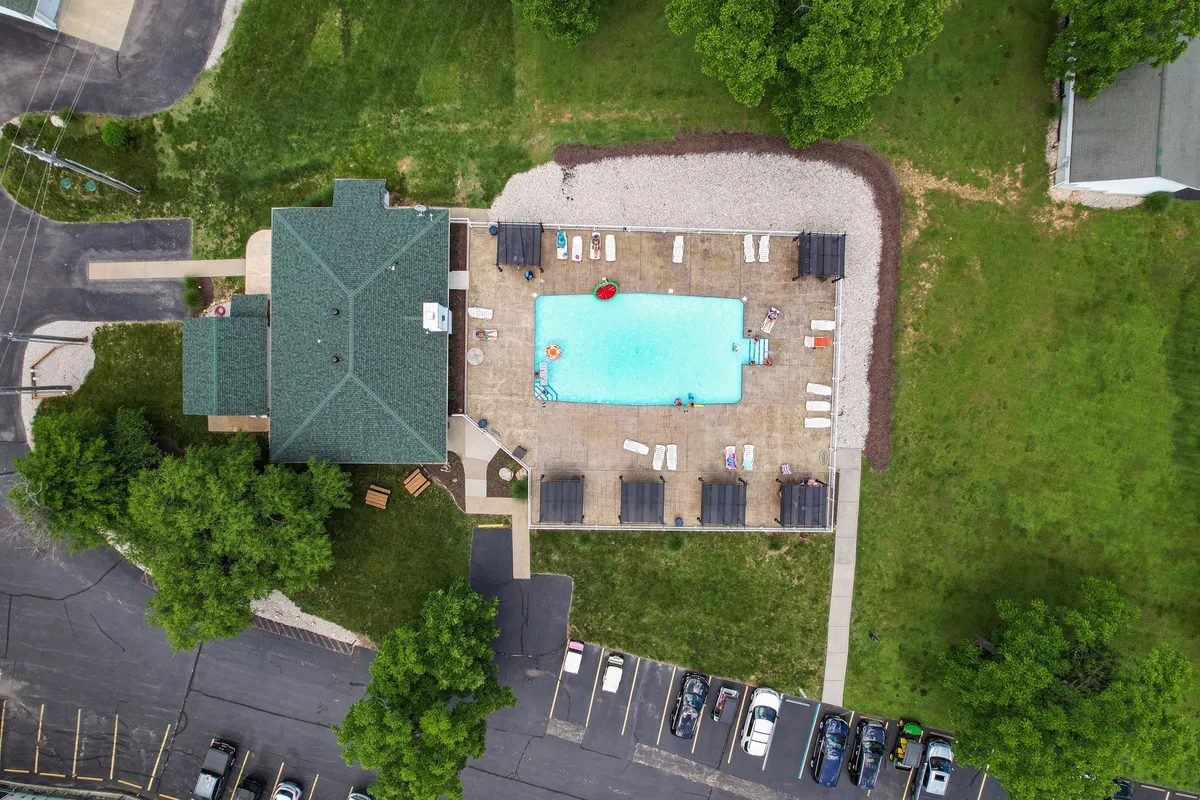 A spacious swimming pool surrounded by lounge chairs and lush greenery, with the building structure in the background. The scene is filled with natural light and offers both sunny and shaded areas for relaxation. The atmosphere is inviting, perfect for group gatherings and leisurely afternoons.