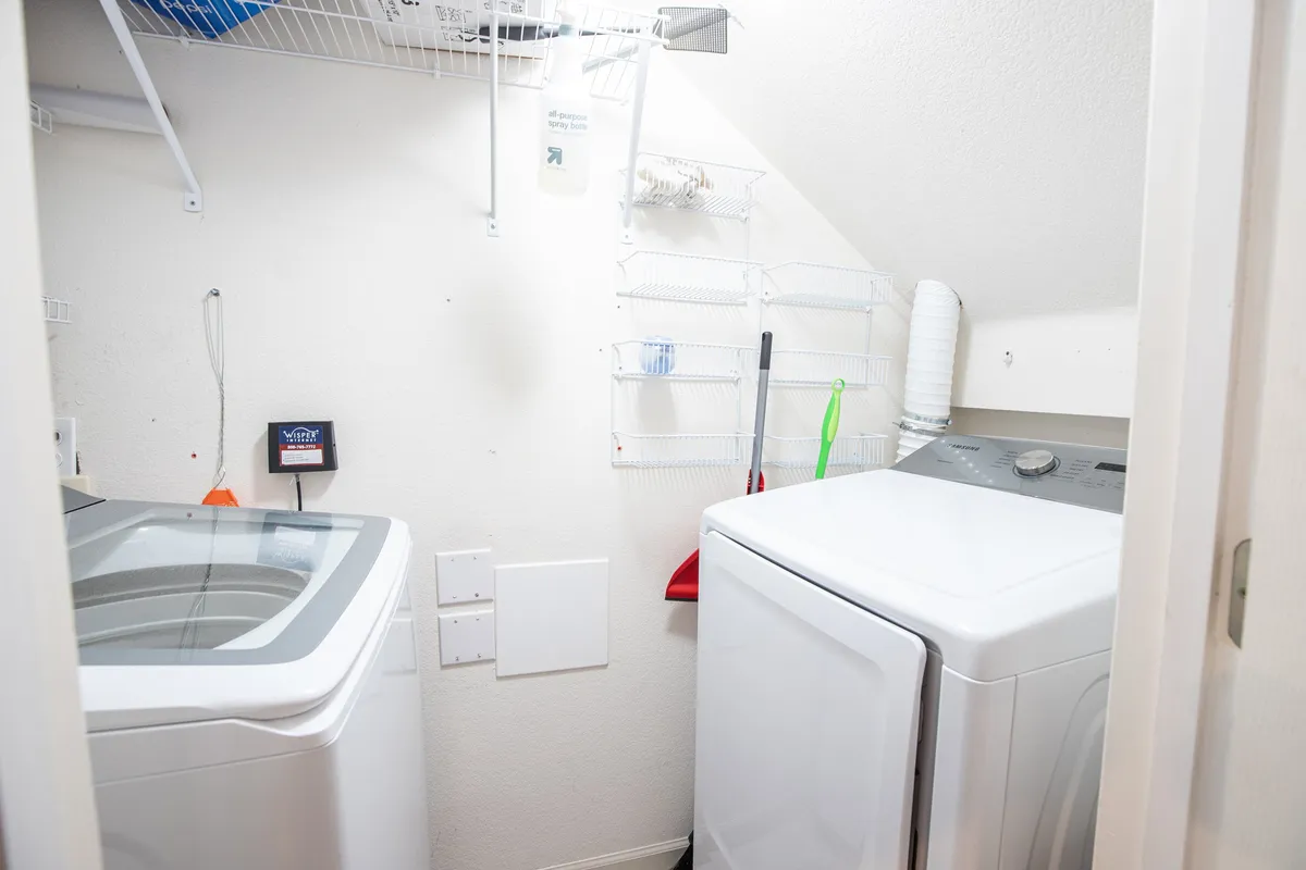 A dedicated laundry room features a washing machine, dryer, and organized shelves for cleaning supplies. The space is clean, practical, and user-friendly, ensuring guests can easily keep their clothes fresh during their stay.